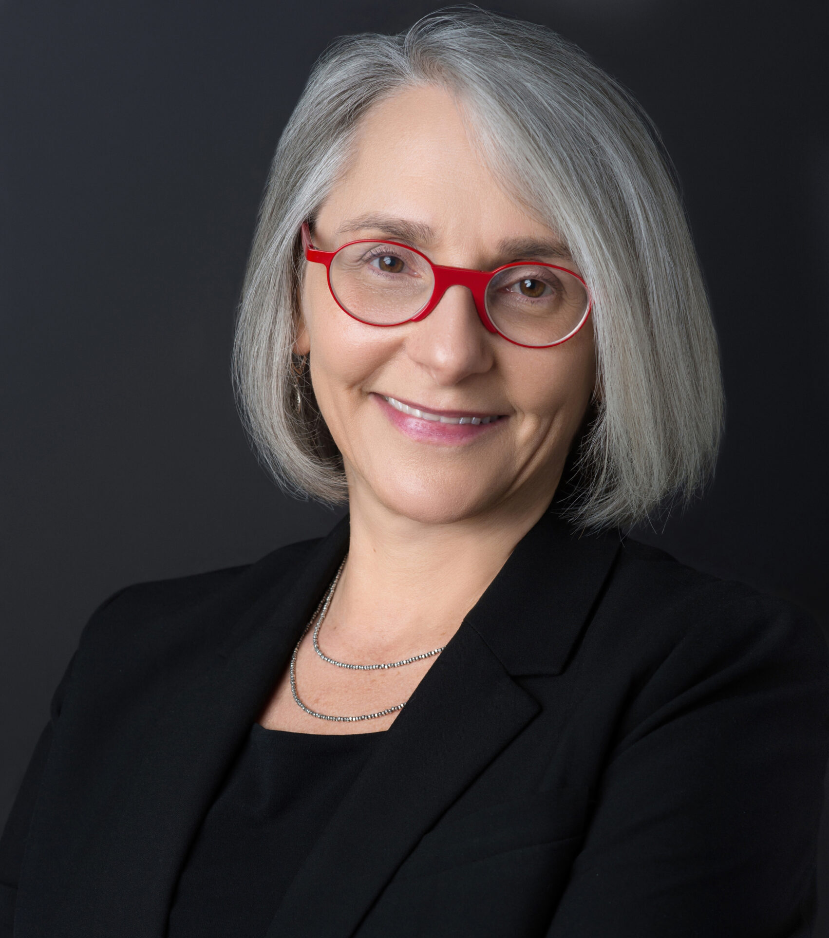 Professor Laura Kessler, a middle-aged woman wearing a dark blazer and round red rimmed glasses smiles for her picture