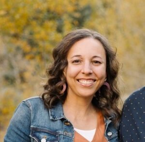 Lindsay Wilcox, a white woman with dark brown hair wearing a jean jacket and brown dress