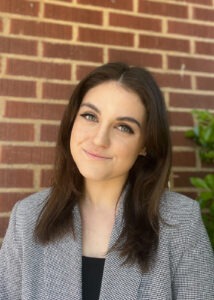 Brooklyn Lindsey, a young white woman with dark brown hair and hazel eyes standing against a brick wall